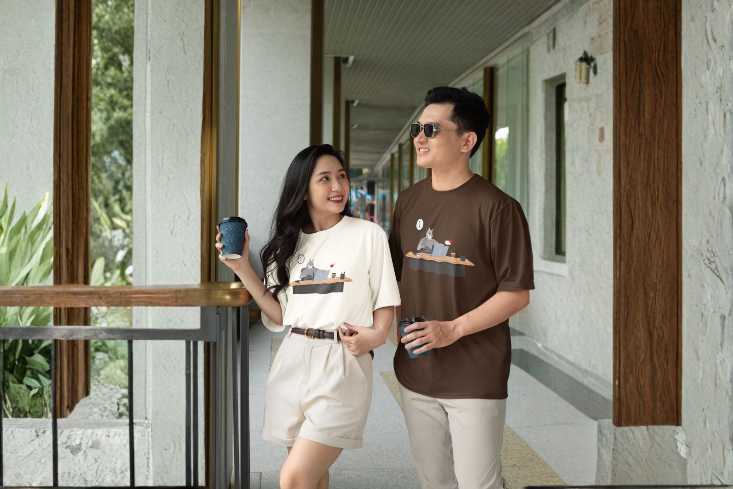 Two people in the Last Minute Task tee, walking a corridor with coffee